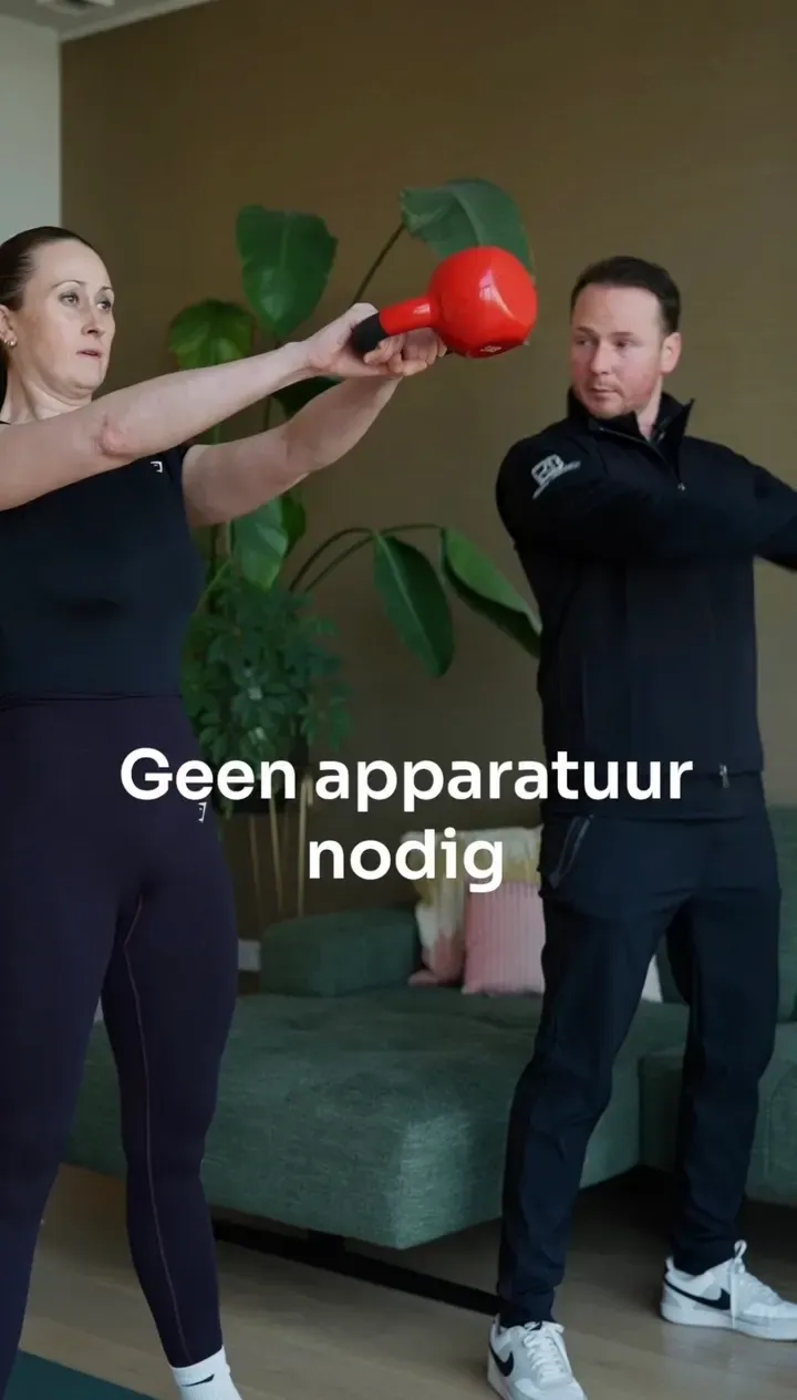 Een personal trainer begeleidt een klant bij een kettlebell-oefening in een woonkamer.